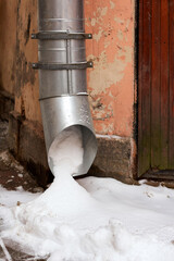 Metal water pipe on the corner of the house is filled with snow