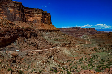 Dirt road at the bottom of the canyon among the layered geological formations of red rocks.