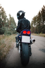Fototapeta premium Rear view of motorcycle driver driving in helmet with blurred forest background