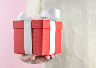 Red box in hand, gift or surprise on a pink background. In the background is an openwork knitted sweater. Concept - Gift for Thanksgiving Day, Birthday, International Women's Day, Caring, Soft Focus