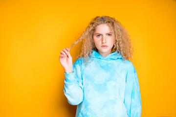 Beautiful girl with curly hair pulls back a lock of hair while standing on a bright background