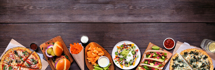 Fototapeta Healthy plant based fast food bottom border. Top view over a dark wood banner background. Table scene with cauliflower crust pizzas, bean burgers, mushroom tacos and vegetarian sides. Copy space. obraz