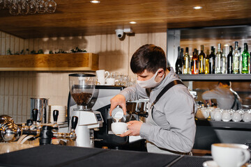 A masked barista prepares delicious coffee at the bar in a cafe. The work of restaurants and cafes during the pandemic.