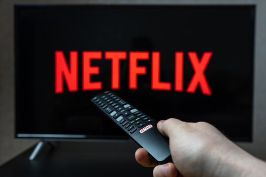 Holding TV remote controller with Netflix logo. Turning on Netflix platform on TV