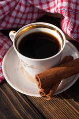 A cup of aromatic black coffee and coffee beans on the table with cinnamon sticks. Morning espresso coffee for breakfast in a beautiful white cup.