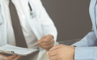 Unknown male doctor and woman-patient discussing current health examination while sitting in clinic and using clipboard. Good medical service in hospital. Medicine concept