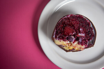 Top view of an opened and cracked red fruits stuffed easter egg on a white plate on a pink background. 