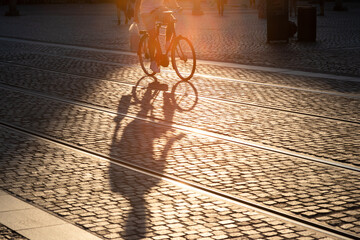 Shadow of a young male riding his bike on historic pavement in a relaxed way during golden hour