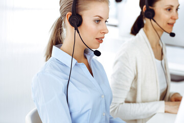 Blond woman call operator is using computer and headset for consulting clients online. Group of...