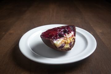 Opened and cracked red fruits stuffed easter egg on a white plate on a wooden table.