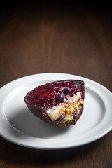 Opened and cracked red fruits stuffed easter egg on a white plate on a wooden table.
