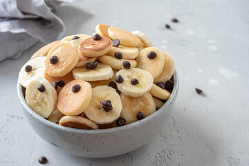 Tiny pancake cereal in a bowl with banana and chocolate chips