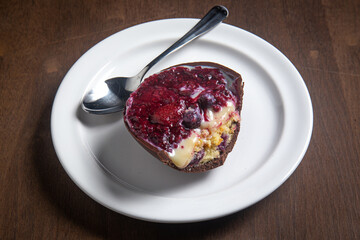 Opened and cracked red fruits stuffed easter egg on a white plate with a spoon on a wooden table.