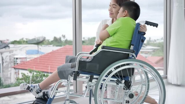 Mother and son with disability on wheelchair at window in home. daily lives care, coexistence. Slow motion shot