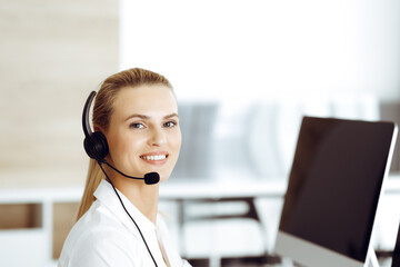 Blond female customer service representative is consulting clients online using headset. Call center and business concept