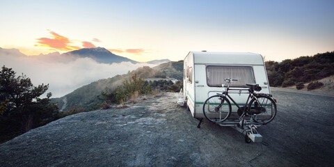 Caravan trailer with a bicycle near mountain lake Lac de serre-poncon in French Alps at sunrise. Golden sunlight, fog. Wanderlust, tourism, landmark, vacations in France. Transportation, RV, lifestyle - 417211910