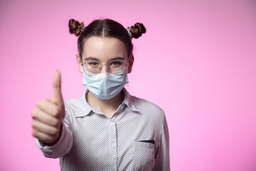 Stylish young teen girl recommending wear medical protective mask against coronavirus showing thumb up on pink backdrop