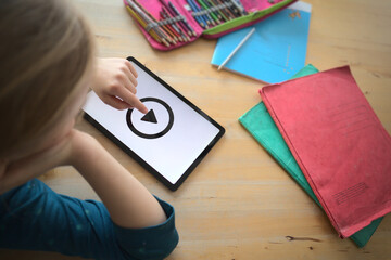 top view on distance learning scene of young girl with tablet computer starting a tutorial video at home with school material surrounding her - home schooling concept with selective focus
