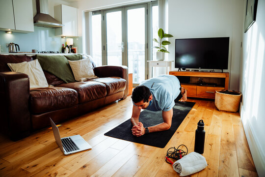 Mixed race male exercising in living room holding plank on floor 