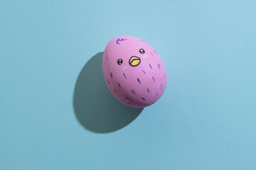 Funny easter egg. Festive decor. Holiday gift. Cute handmade art. Pink egg with painted chicken pattern isolated on blue textured copy space.