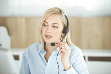 Blonde business woman sitting and communicated by headset in call center office. Concept of telesales business or home office occupation