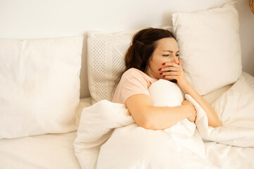 beautiful young woman lies on bed under the covers with a cold 