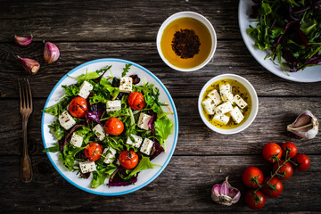 Fresh vegetable salad with feta cheese, tomatoes, arugula, lettuce and roast tomatoes on wooden table
