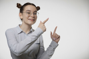 Modern positive young girl in glasses pointing fingers aside at copy space for text advertisement eyewear store