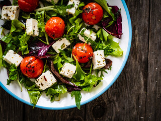 Fresh vegetable salad with feta cheese, tomatoes, arugula, lettuce and roast tomatoes on wooden table
