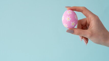 Spring craft. Easter ornament. Holiday decoration. Painted pink egg with white yellow flower pattern in woman hand isolated on blue empty space background.