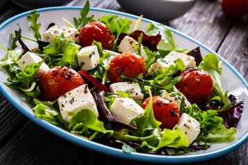 Fresh vegetable salad with feta cheese, tomatoes, arugula, lettuce and roast tomatoes on wooden table
