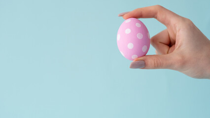 Easter ornament. Festive decoration. Spring holiday gift. Pink white spotted color egg with polka dot minimal pattern in female hand isolated on blue empty space background.