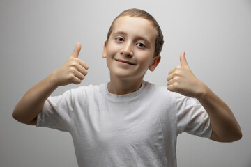 Positive child boy showing thumbs up, like hands gesture on gray studio background with copy space for advertising