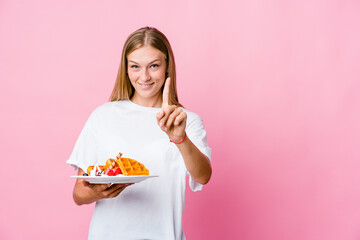 Young russian woman eating a waffle isolated showing number one with finger.