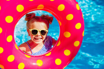 a happy little girl in sunglasses holds a swimming circle near the pool in the summer. space for text. children's summer holidays