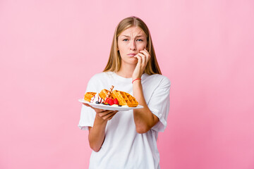 Young russian woman eating a waffle isolated biting fingernails, nervous and very anxious.