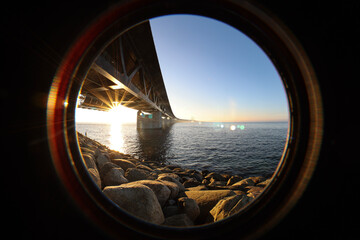 Inside lens view of the Sun under the Oresund bridge Sweden side at the viewpoint near Limhamn, February 2021. Wide angle, clear sky, bridge stretching from the near left to the horizon.