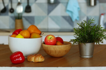 fruit in bowl still life with pot plant, paprika and croissant on the table close up photo on blue kitchen background