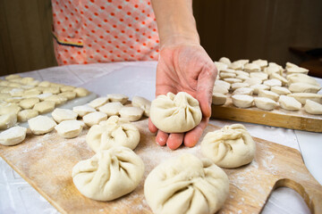 Woman's hand soiled with flour hold khinkale dumpling on the background of cutting boards with hendmade dumplings, ravioli and khinkali.