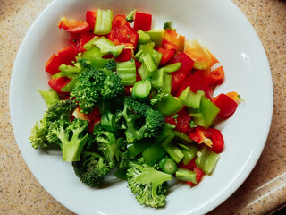 fresh red sweet pepper and green broccoli diced on a white plate ready for salad or cooking. Vegetarian diet