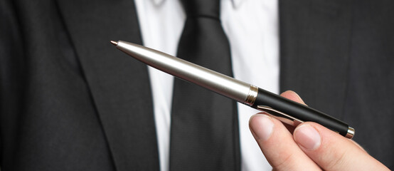 Businessman giving pen for your signature on clipboard