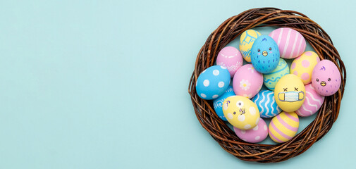 Easter banner. Pandemic holiday. Handmade food ornament. Cute pastel color painted egg in protective face mask with chicken bunny pattern in basket isolated on blue copy space conceptual background.