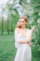 Portrait of a young woman in the spring in the park in a white boudoir dress