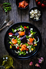 Salmon salad - smoked salmon with feta cheese, avocado and mix of vegetables on wooden table
