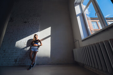 Beautiful contrasting portrait with the play of light and shadow of a young and fit girl in a loft interior with a white brick wall