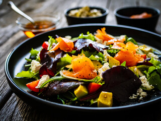 Salmon salad - smoked salmon with feta cheese, avocado and mix of vegetables on wooden table
