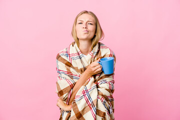Obraz na płótnie Canvas Young russian woman wrapped in a blanket drinking coffee frowning face in displeasure, keeps arms folded.