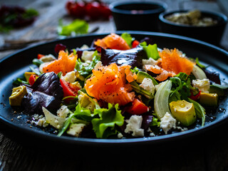 Salmon salad - smoked salmon with feta cheese, avocado and mix of vegetables on wooden table
