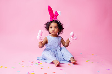 portrait of a cute little girl with Easter bunny ears on her head holding Easter eggs. studio, pink background