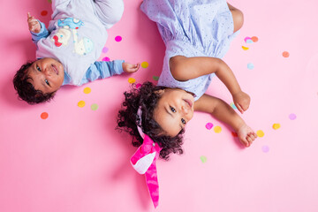 Obraz na płótnie Canvas two charming little girls with dark skin and curly hair in beautiful dresses are lying on the floor in confetti